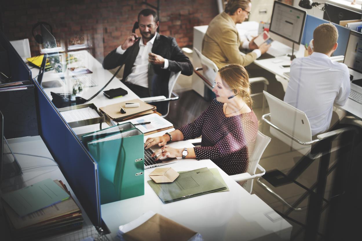 4 people working in an office setting surrounded by computers and telephones