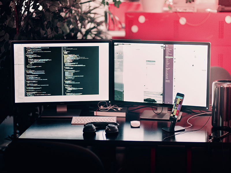 desk with two screens, keyboard headphones and a phone on