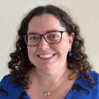 person with long curly hair and glasses smiling for the camera